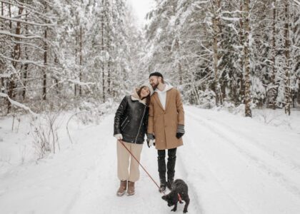 Couple enjoying a winter walk with their dog in a snow-covered forest.