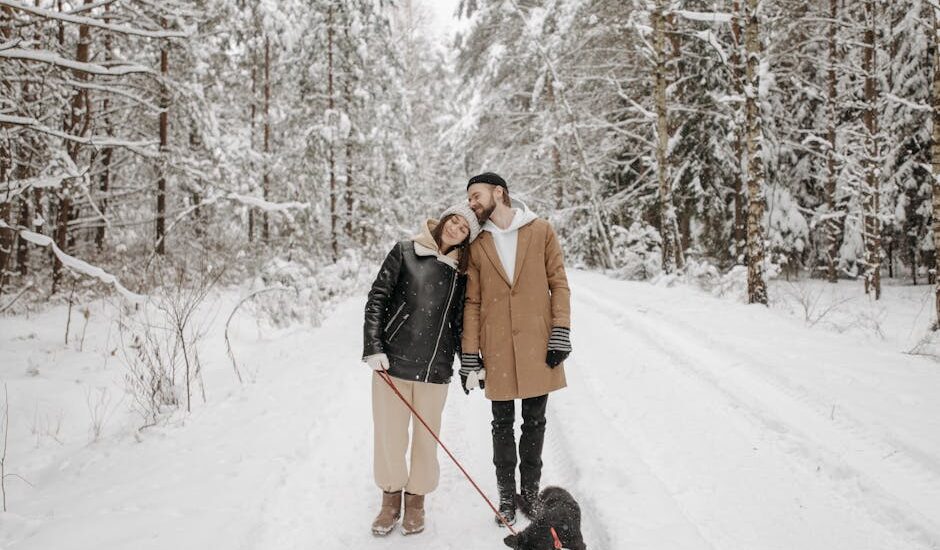 Couple enjoying a winter walk with their dog in a snow-covered forest.