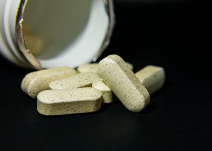 Several beige dog vitamin tablets spilled from an open bottle, illustrating the risks of dogs overdosing on supplements.