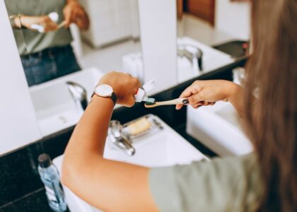 A woman is applying toothpaste to a toothbrush in a bathroom setting, showing daily oral hygiene habits.