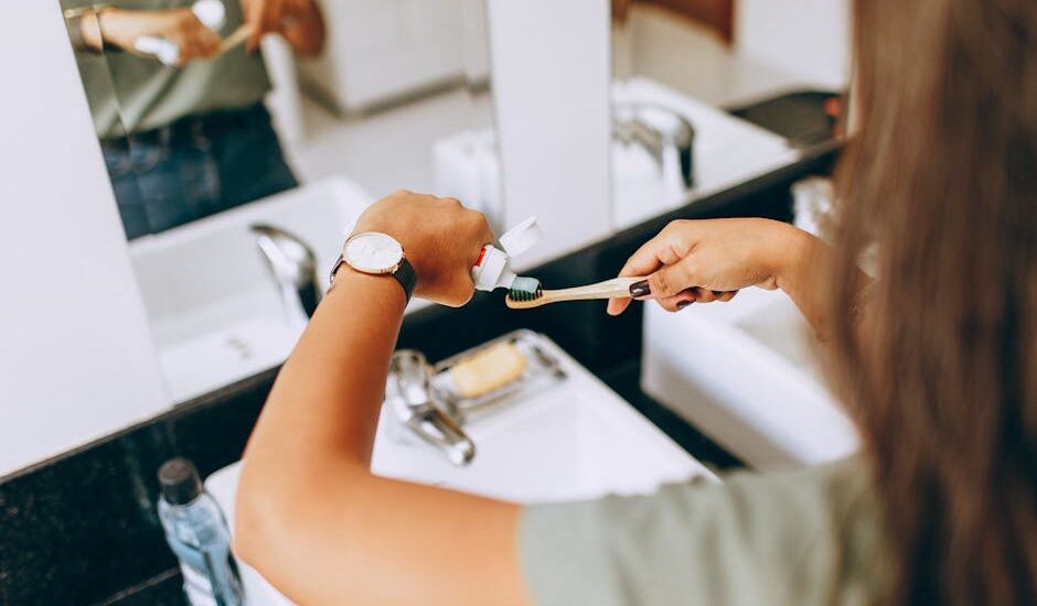 A woman is applying toothpaste to a toothbrush in a bathroom setting, showing daily oral hygiene habits.
