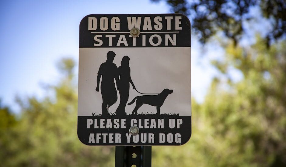 A dog waste station sign in a park reminding pet owners to clean up after their dogs.