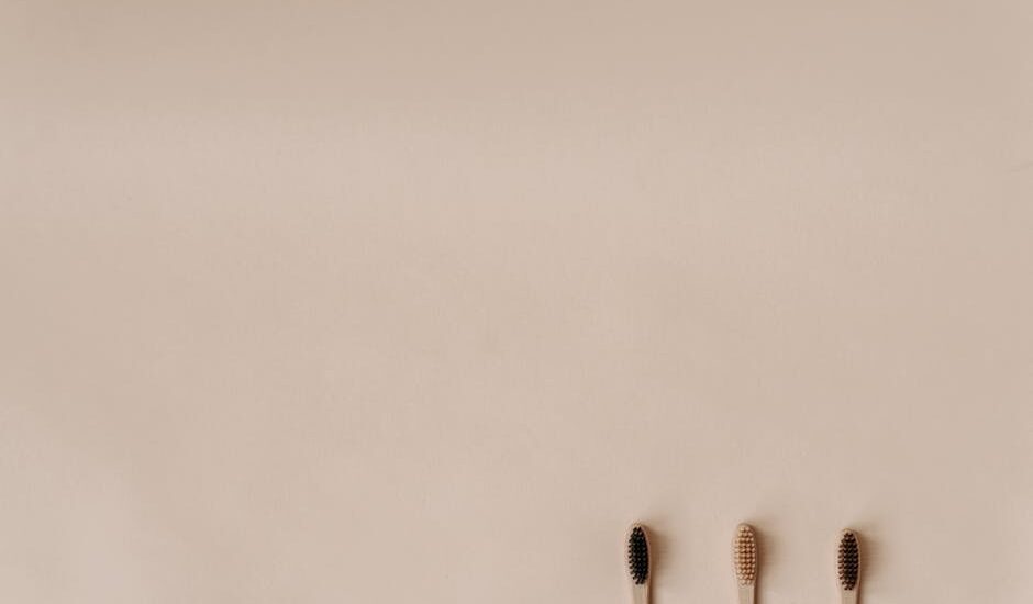 Three bamboo toothbrushes on a minimal beige background promoting eco-friendly oral care.
