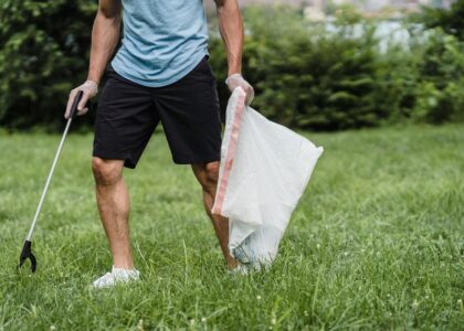 Person cleaning up after a dog walk with a grabber-style poop scooper and plastic bag in a grassy park area.