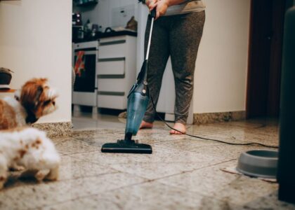 A person vacuums a floor while a small dog watches, highlighting deshedding vacuums.