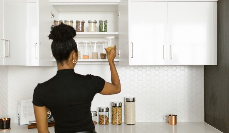 A person reaching for a clear container in a kitchen cabinet, showcasing dog food storage options.